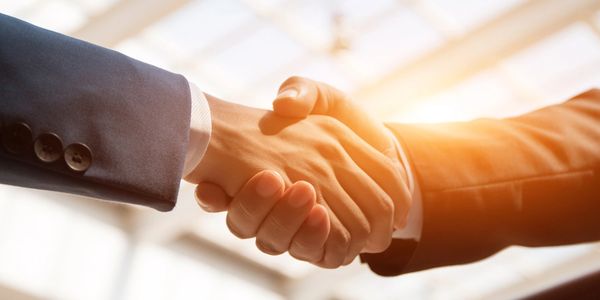 Two people shaking hands, picture shows from mid forearm to clasped hands, both in business suits.