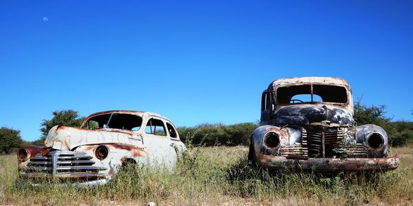 Two old rusty car wrecks sitting in a paddock.