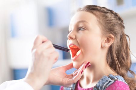 pediatric urgent care doctor examining little girl's sore throat with penlight