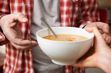  A person handing another person a bowl of soup.