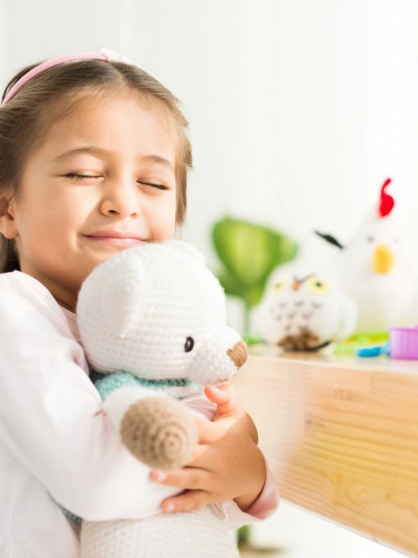 Young girl giving a soft teddy a hug, with eyes closed and a big smile
