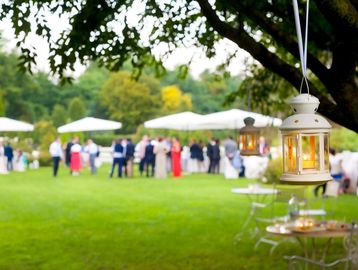An outdoor event space with guests mingling on vibrant green grass among tents, trees, and decor.