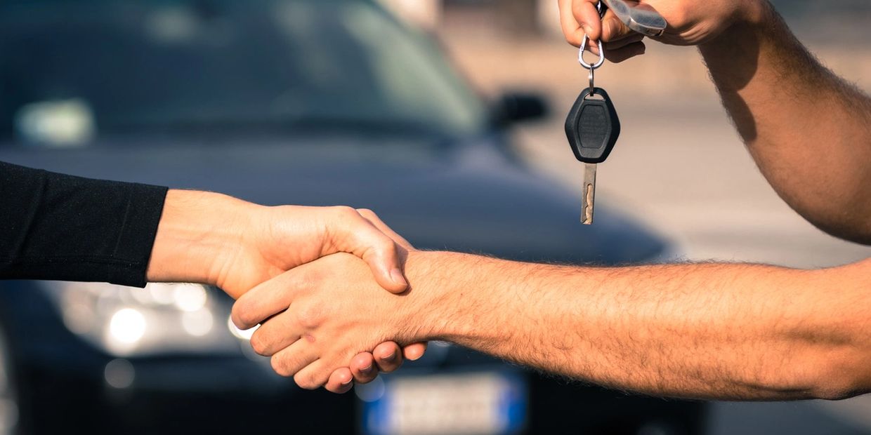 two people shaking hands and handing a key over with a car in the background