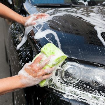 side shot of a black sedan getting detailed with soap on it and a person wiping it down