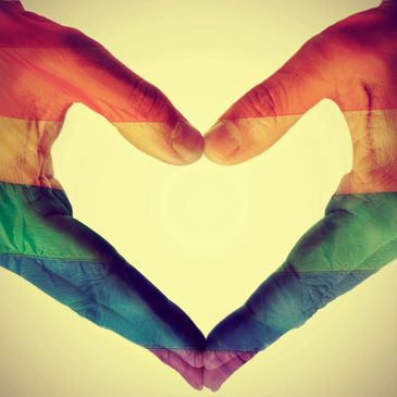 Hands forming a heart with an LGBT pride flag in front of a yellow background.