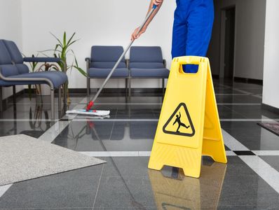 Wet floor sign in foreground, man sweeping floor in background