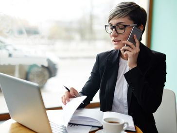 A buy realtor on the phone with a client looking at her laptop with on a cluttered desk