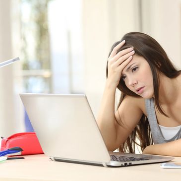 Teen age girl looking at a computer screen with her hand on her forehead.