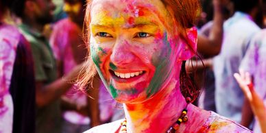 A young girl at a festival smiling because she has her face rainbow colored. 