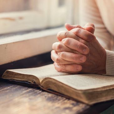Person with clenched hands praying over an open bible
