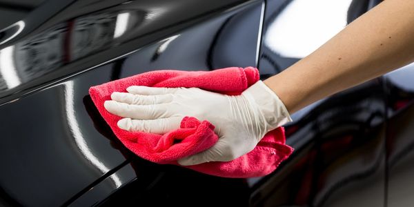 A gloved hand is buffing a black car hood to a polished sheen