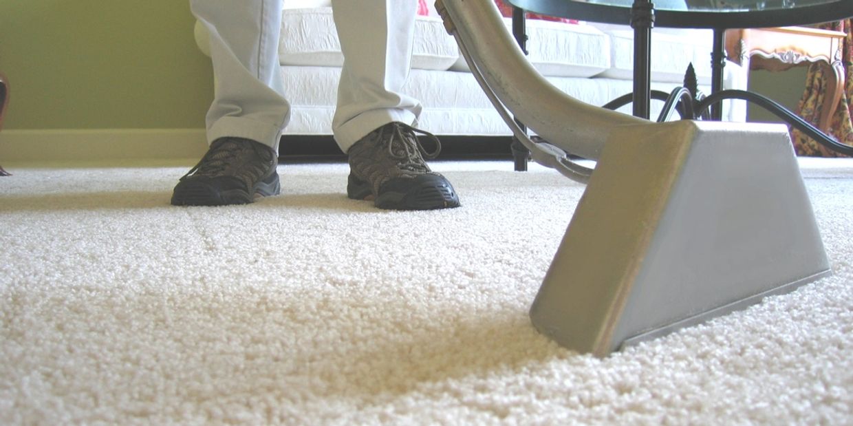 A professional carpet cleaner is using a extraction wand to remove water and dirt from a carpet.