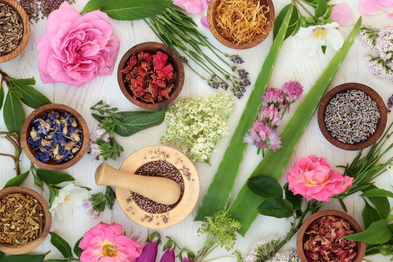 Image of dried herbs in small wooden bowls, flowers, and mortar and pestle.
