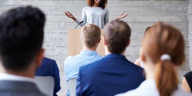 A woman speaking to an audience on a podium