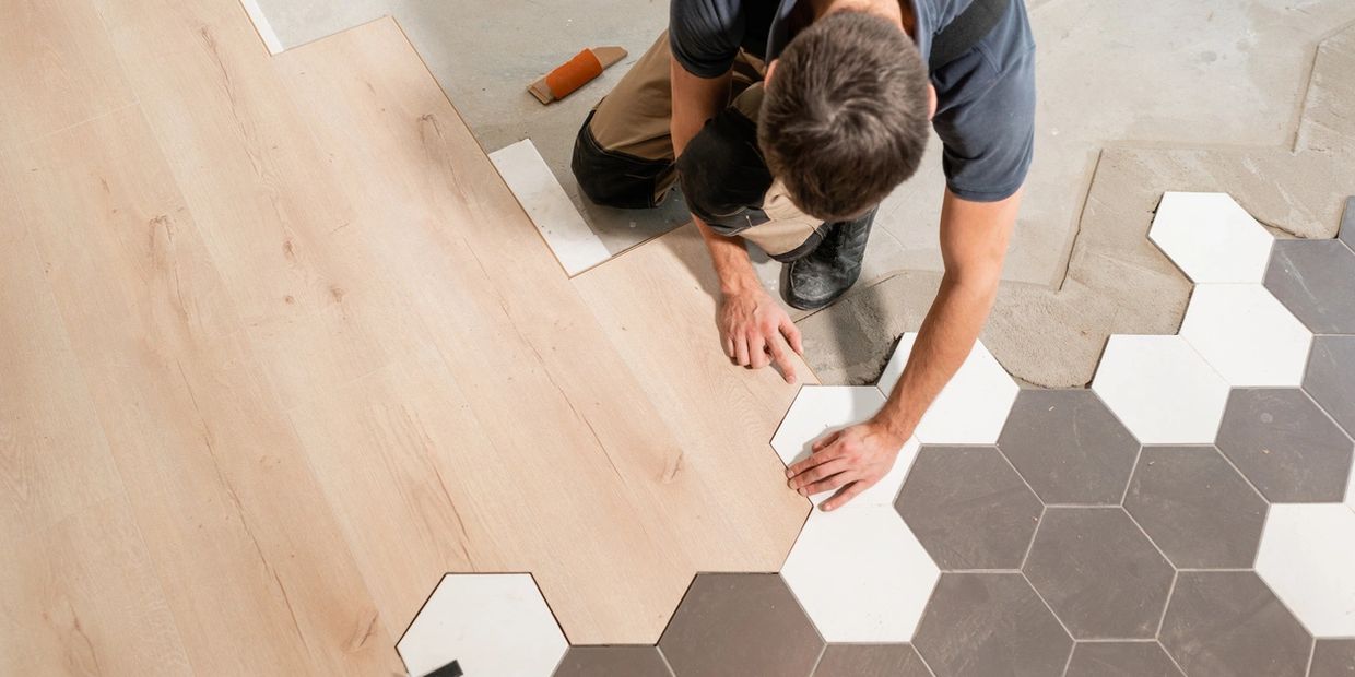 A flooring installer lays down a hardwood floor and connects it to hexagon tiles.