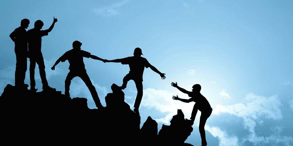 Group of people helping each other get up a rocky hilltop