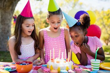 Kids gathered around a birthday cake with food and birthday party decorations. 