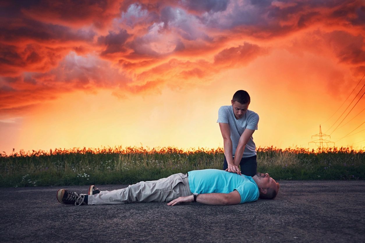 A person is performing CPR on an unresponsive gentleman lying on the ground.