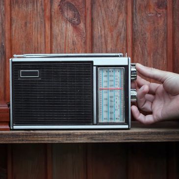 Old fashioned radio being adjusted by a person's hand on the dial