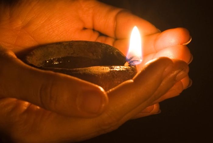 Hand holding small clay dish of oil and 2 lit wicks creating one flame