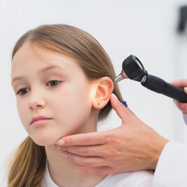 A doctor looking at a girls year. Ear infections can be helped with chiropractic. 