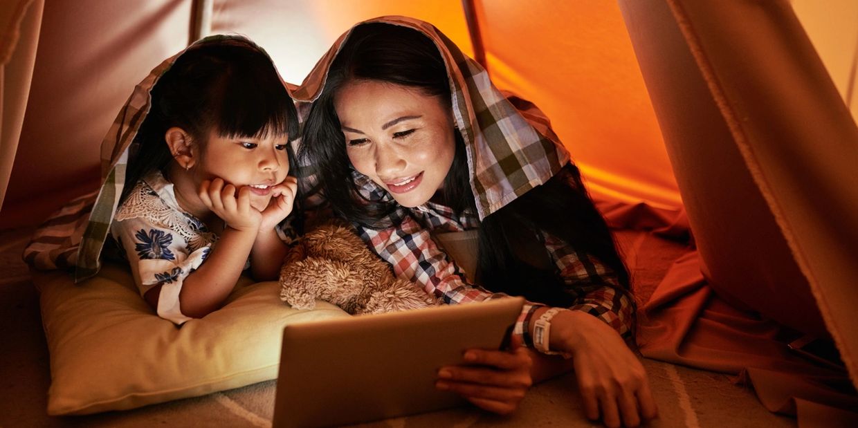Asian mom and daughter in tent looking at laptop