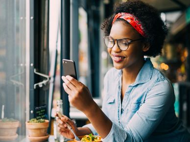 Black woman smiling at her cell phone in a restaurant