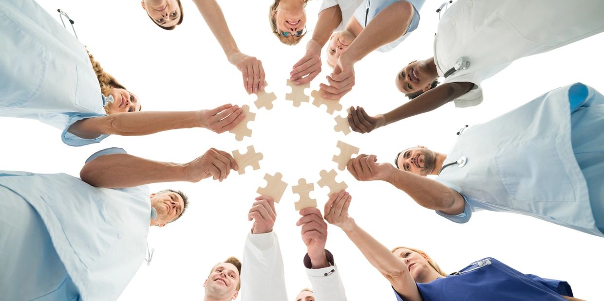 Healthcare workers holding puzzle pieces in a circle.  