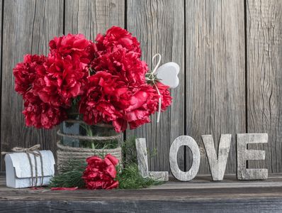 red flowers in glass vase with Love in letters resting on a surface