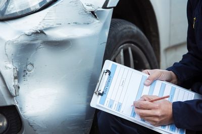 Person inspecting damaged vehicle and making a repair estimate