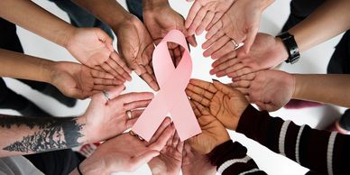 Group of people putting their hands together to hold a breast cancer ribbon