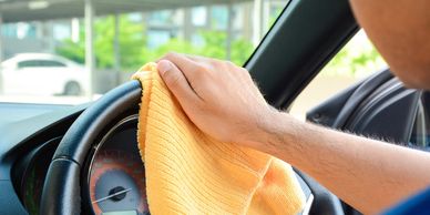 Person using a cloth rag to clean the inside of a car steering wheel.