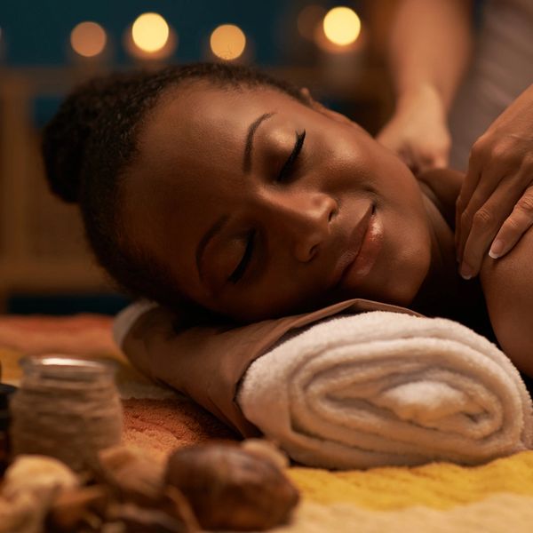 A black lady with a smiling face, getting a relaxing massage, relieving pain on the shoulders. 