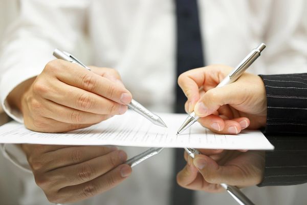 Two people holding pens and pointing on the paper