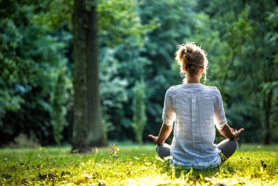 woman sitting crossed legged looking out to the forest in a meditative pose with hands up on knees.