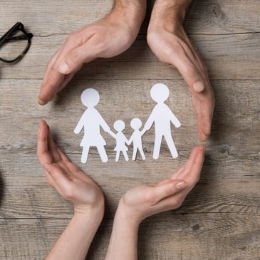 Paper cut out of family encircled by hands.