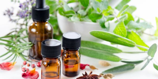 Three bottles of essential oils beside array of herbs