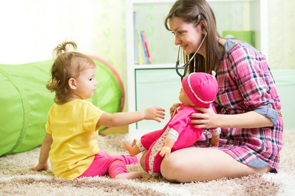 Mother and infant daughter pretend playing with baby doll and medical toys