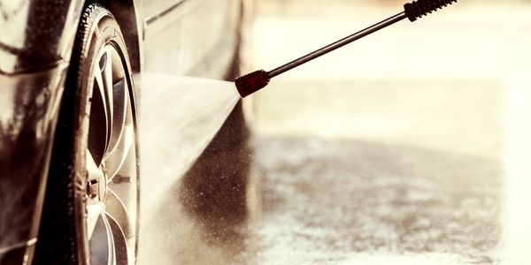A powerwasher sprays water onto a car wheel.