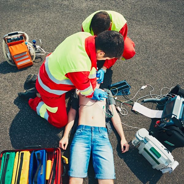 2 paramedics attempting CPR with defibrillator on a young male.