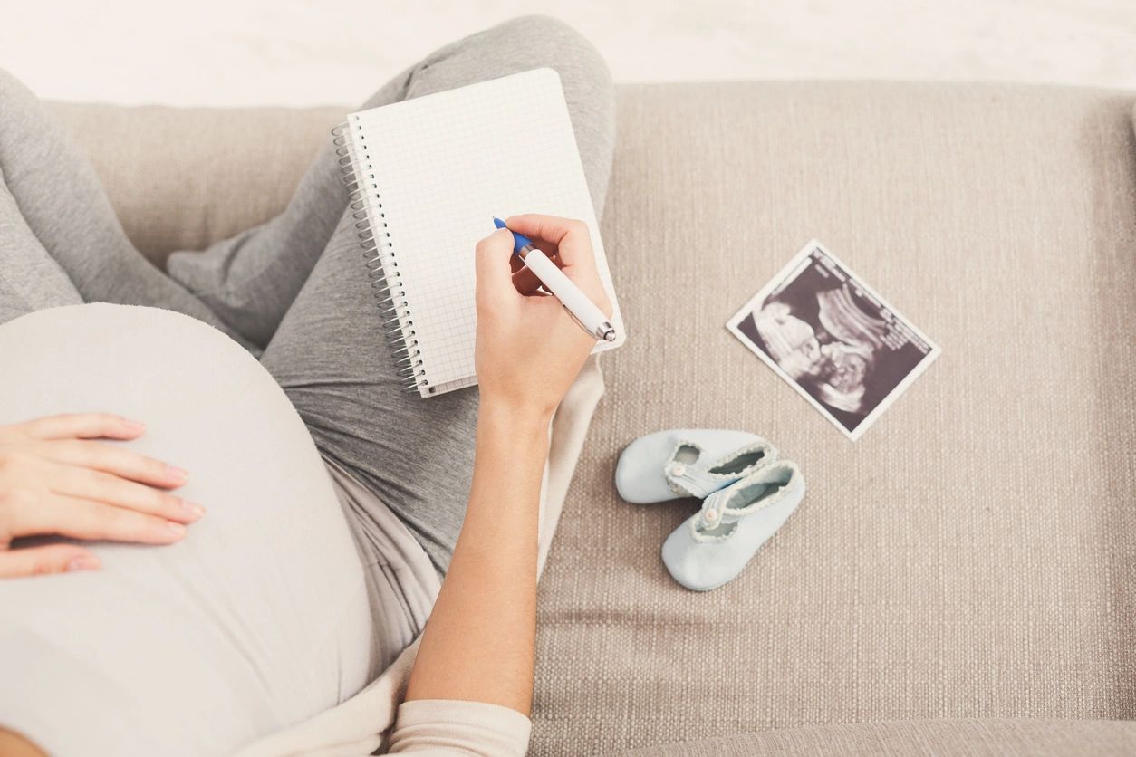 Pregnant mom writing notes while looking at baby booties and sonogram 