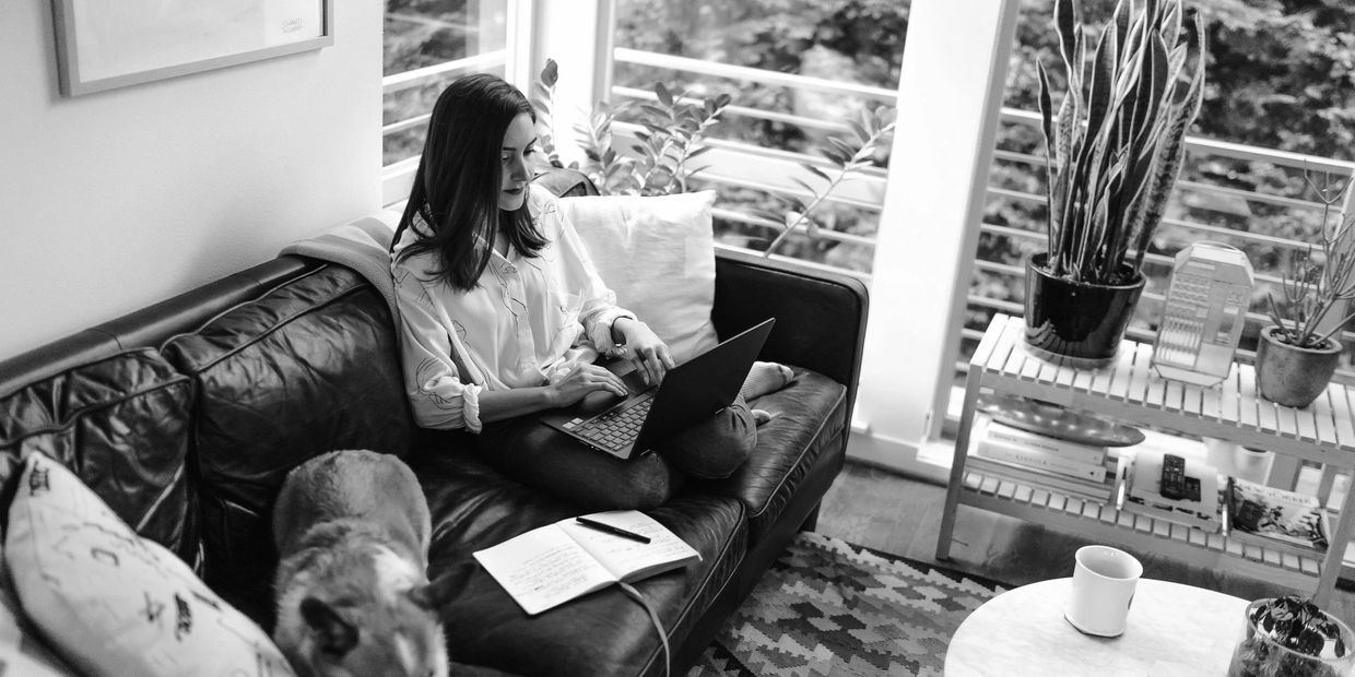A young woman with straight dark hair sitting on a couch with a laptop on her lap.