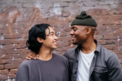 Two masculine people turned towards each other, smiling.