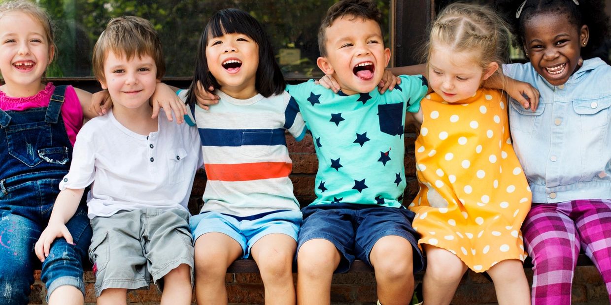 6 Kinder die lachen und auf einer Mauer sitzen