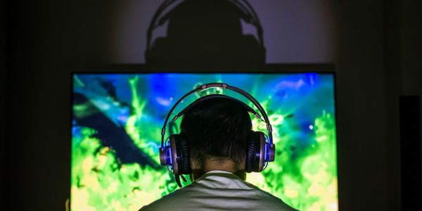A man wearing a gaming headset in front of his monitor.