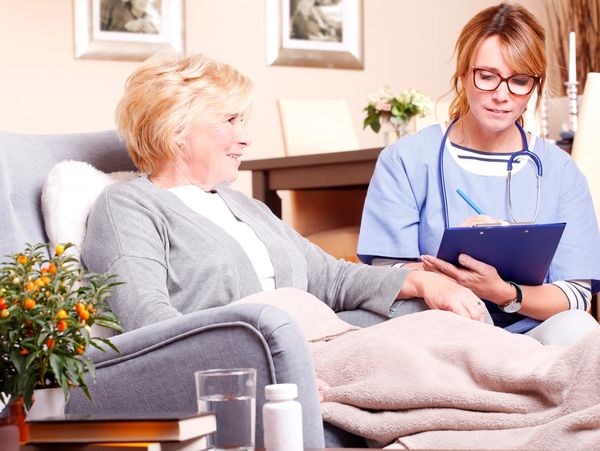 elderly woman sitting in a recliner with a nurse sitting next to her talking to each other