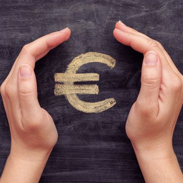 Ein € (Euro-Zeichen) auf einer Kreidetafel, die zwischen zwei Händen eingeklemmt ist