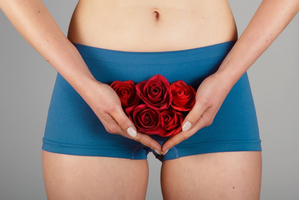 Woman in blue exercise shorts holding euphemistic roses over uterus, vagina area for Pelvic Health