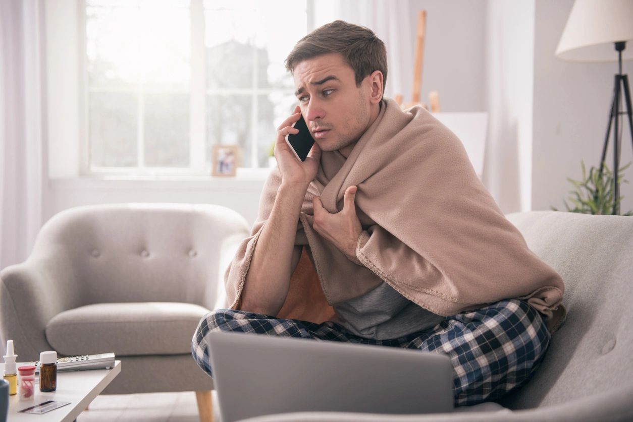 A man sitting on a couch with a blanket wrapped around his shoulders