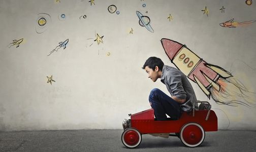 young man squeezed into toy car with rocket drawing behind